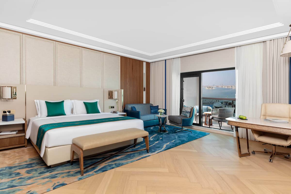 A hotel room with a large bed, a desk, a chair, and a view of the city.