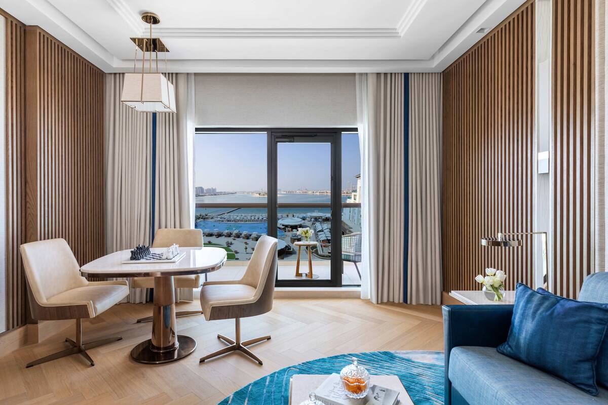 A modern hotel room with a dining area, a sofa, and a view of the sea.