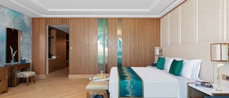 A modern hotel room with a large bed, a desk, a chair, a small table with apples, and a TV.