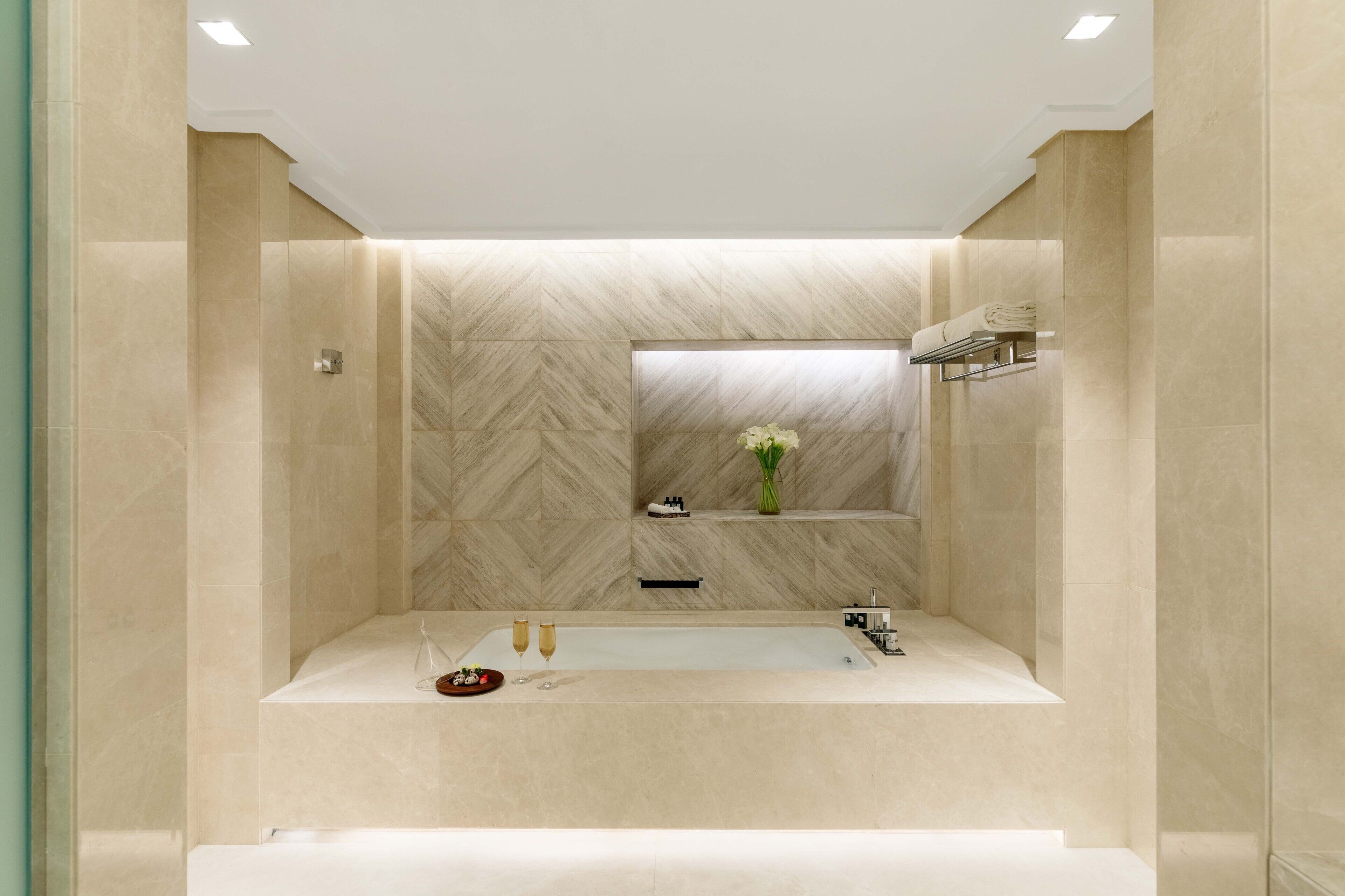 A modern bathroom with a large bathtub, a mirror, and a shelf with toiletries.