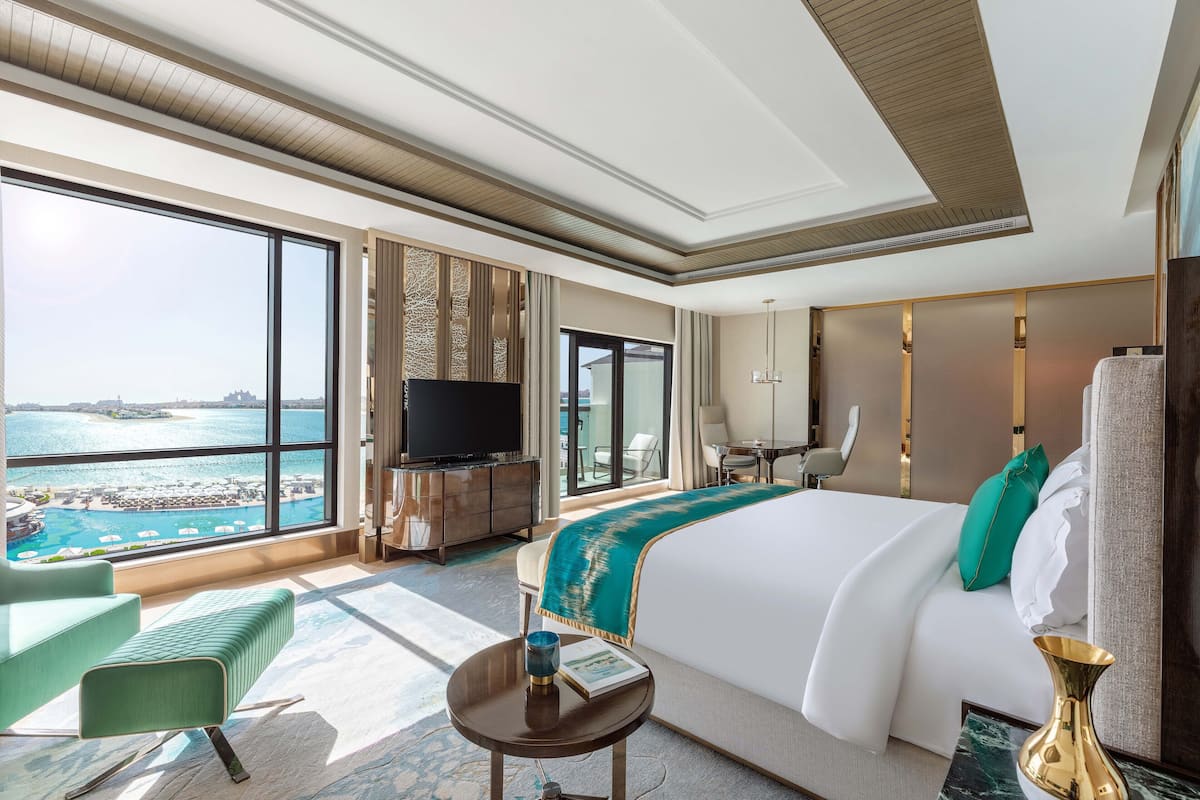 A hotel room with a large bed, a TV, a desk, and a view of the ocean.
