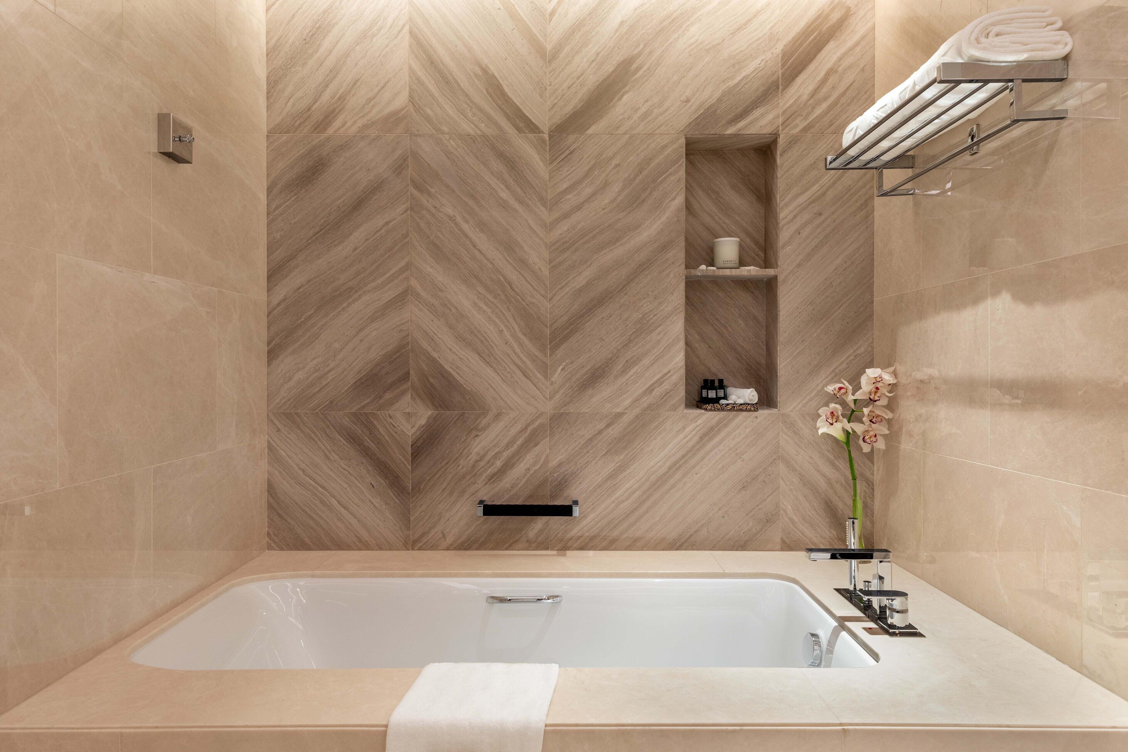 A modern bathroom with a large bathtub, a towel rack, and a small shelf with toiletries.