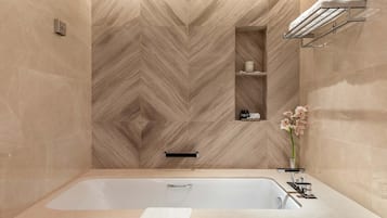A modern bathroom with a large bathtub, a towel rack, and a small shelf with toiletries.