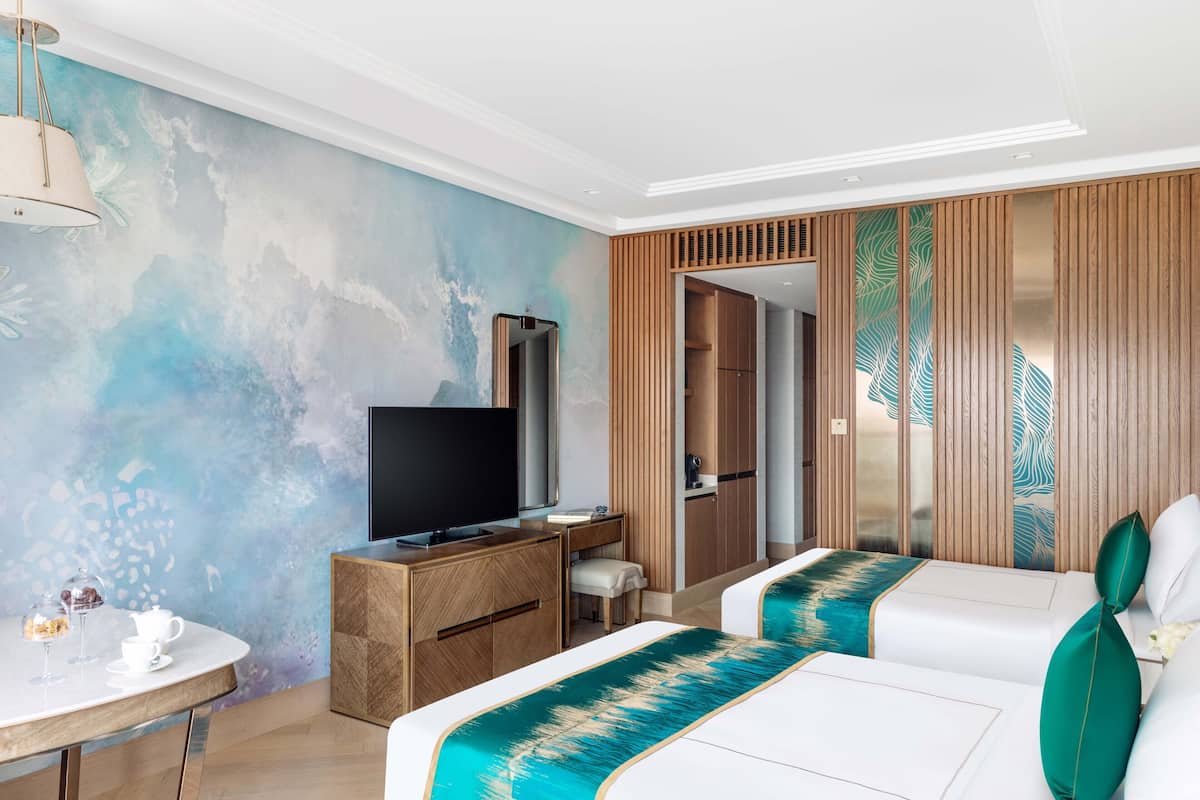 A modern hotel room with a large bed, a desk with a TV, a small table with a teapot, and a wardrobe.