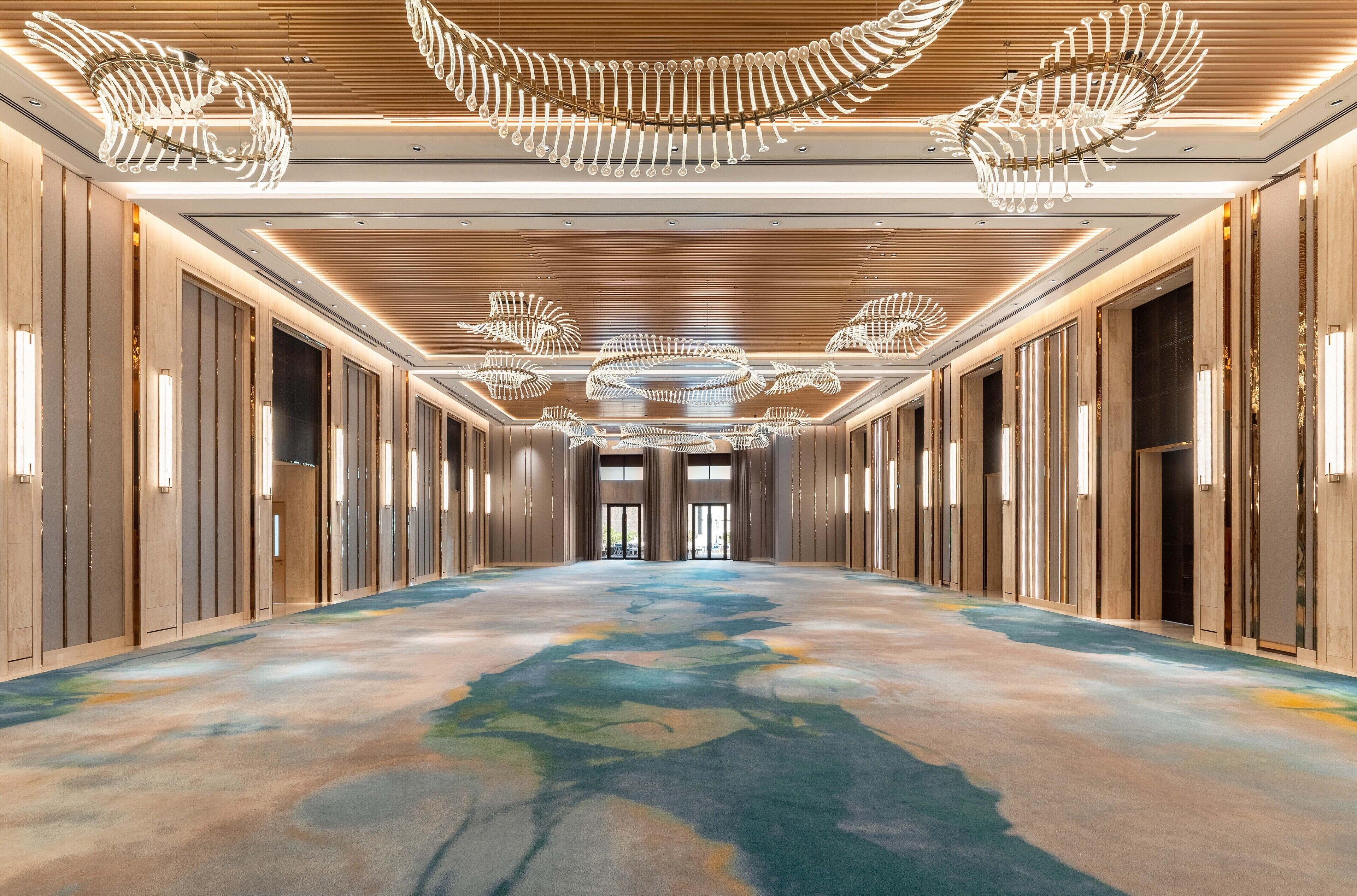 A long, well-lit hallway with modern chandeliers and a colorful floor design.
