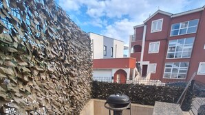 A patio with a barbecue grill, a wooden deck, a stone wall, and a building in the background. - Apartment in Okrug Gornji with Terrace, Air condition, WIFI, Washing machine (5070-1) (Okrug Gornji)