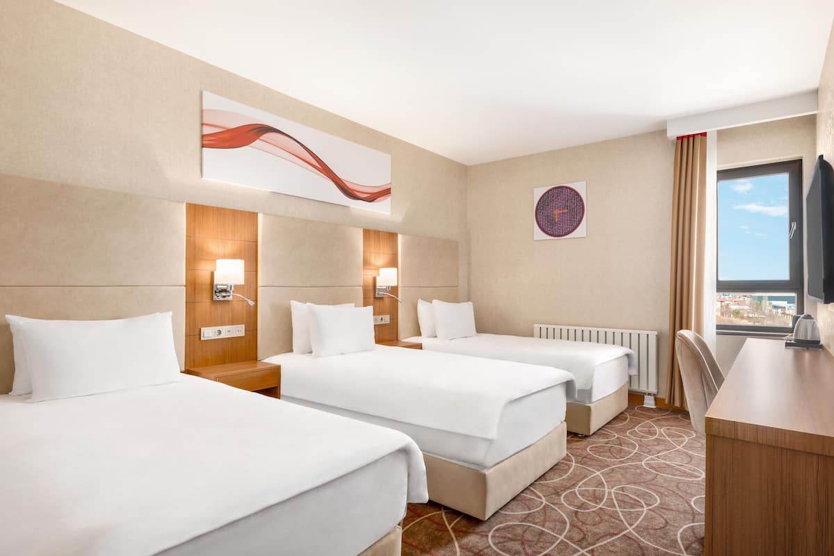 Een hotelkamer met drie enkele bedden, een bureau en een televisie.