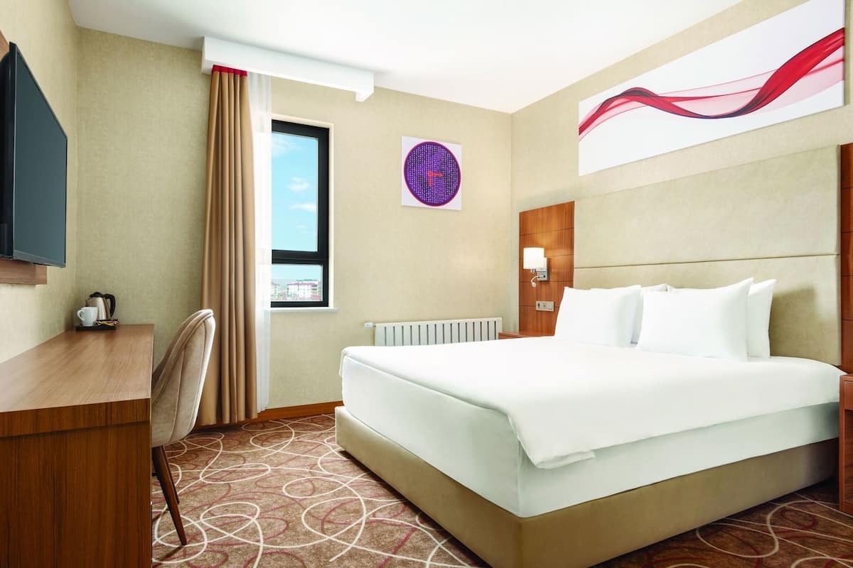 Hotelkamer met een bed, bureau, stoel, klok en raam met uitzicht.