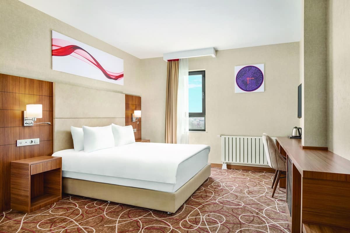 Een hotelkamer met een bed, nachtkastjes, een bureau, een radiator en kunst aan de muur.