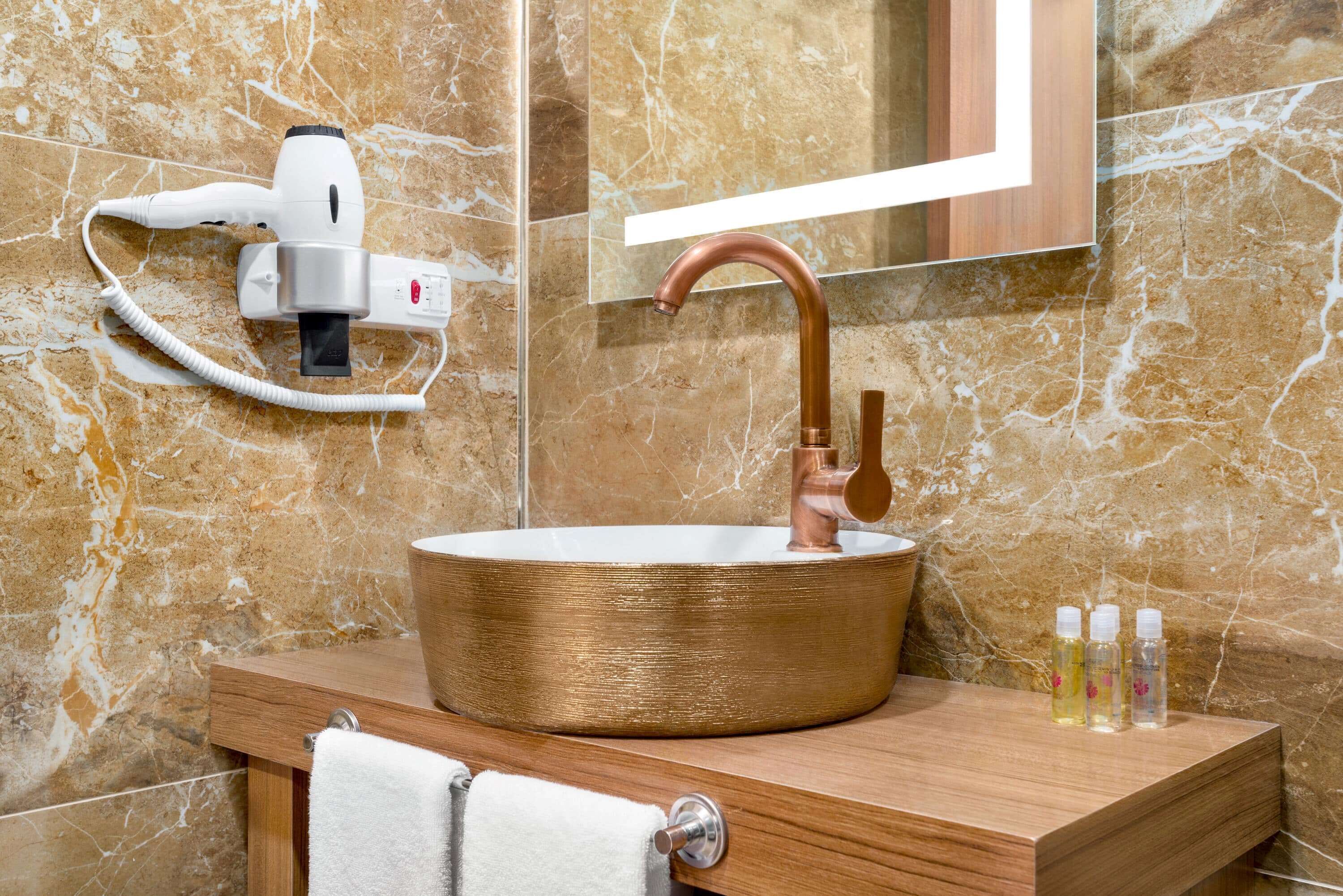 A bathroom with a copper sink, a hairdryer, and three bottles of liquid on the vanity.