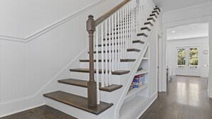 Eine Treppe mit Holzsitzstufen und weißen Geländern, die zu einer Zwischenebene mit einer Tür und einem Blick ins Freie führt.