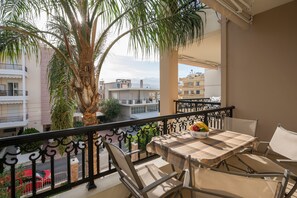 A balcony with a table and chairs, a palm tree, and a view of buildings. - Holiday apartment, lovely balcony mountain view (Chania)