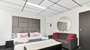 A modern hotel room with a bed, a sofa, a round mirror, and a door. - The Mac Boutique Hotel (Adelaide)