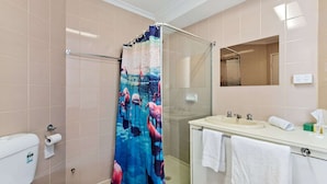 A bathroom with a glass shower enclosure, a toilet, a sink with a mirror, and two towels. - The Mac Boutique Hotel (Adelaide)