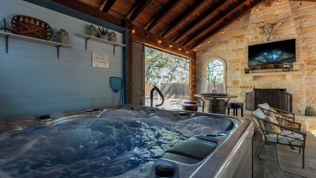 Un jacuzzi en una habitación rústica con paredes de piedra, vigas de madera y una chimenea de piedra, además de estantes con objetos decorativos.