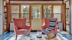 Una habitación acogedora con dos sillones rosa, techo de madera y un amplio ventanal con vistas a árboles.
