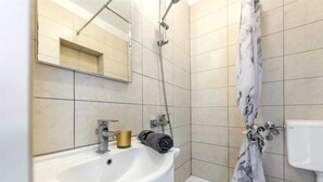 Et badeværelse med en hvid vask, et spejl, en bruser med marmardrapering og et toilet.