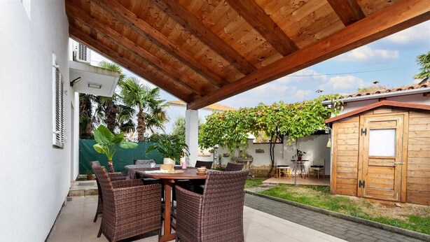 En udendørs patio med fletmøbler, en træpergola og et lille skur i træ.