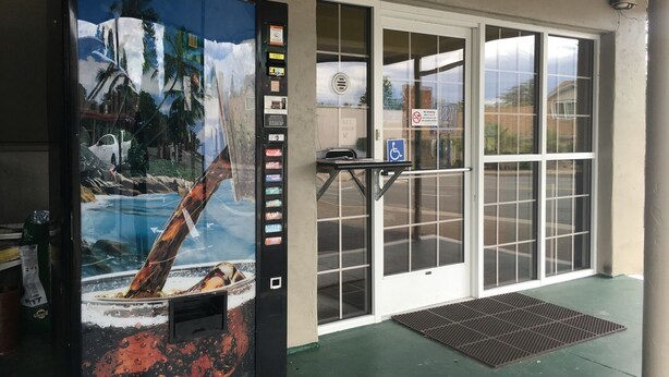 Una máquina expendedora con un mural tropical, una entrada accesible para sillas de ruedas y un letrero de prohibido fumar.