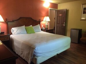 A neatly made bed with a wooden headboard, two bedside lamps, and a door with a number plate. - Budget Inn (Redding)