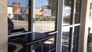 Entrada de hotel con puerta de vidrio, cartel de prohibido fumar y vista de la calle y edificios.