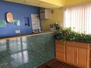 A reception area with a marble counter, a wall-mounted clock, a calendar, and a plant. - Budget Inn (Redding)