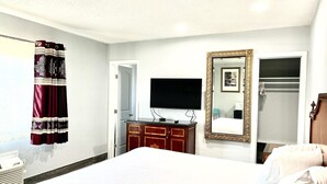 Una habitación de hotel con una cama, televisión, cómoda, espejo y armario.