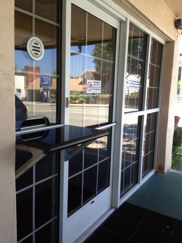 A hotel entrance with a glass door, a no-smoking sign, and a view of the street and other buildings. - Budget Inn (Redding)
