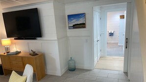 A living room with a TV, wooden cabinet, and a chair with a checkered cushion. - Charming and cozy apartment nestled in the woods. (Mount Desert)