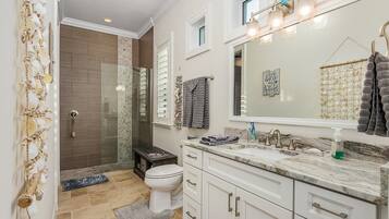 A bathroom with a glass shower, a toilet, a sink with a mirror, and a towel rack.
