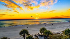 Ein Strand mit Sonnenuntergang, Palmen und einigen Spaziergängern.