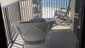 Ein Balkon mit Korbmöbeln, einem Metallgeländer und Blick auf Strand und Meer.