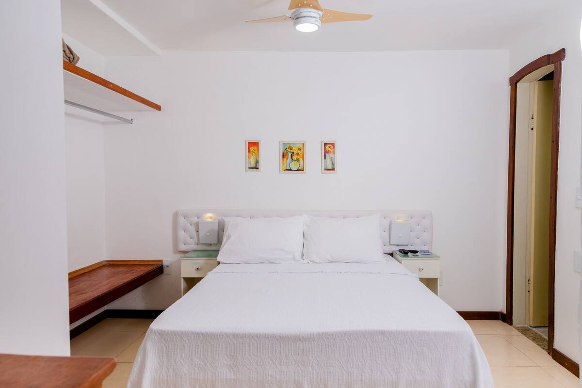 Une chambre à coucher comprenant un lit, des tables de chevet, une commode, un ventilateur de plafond et une porte.