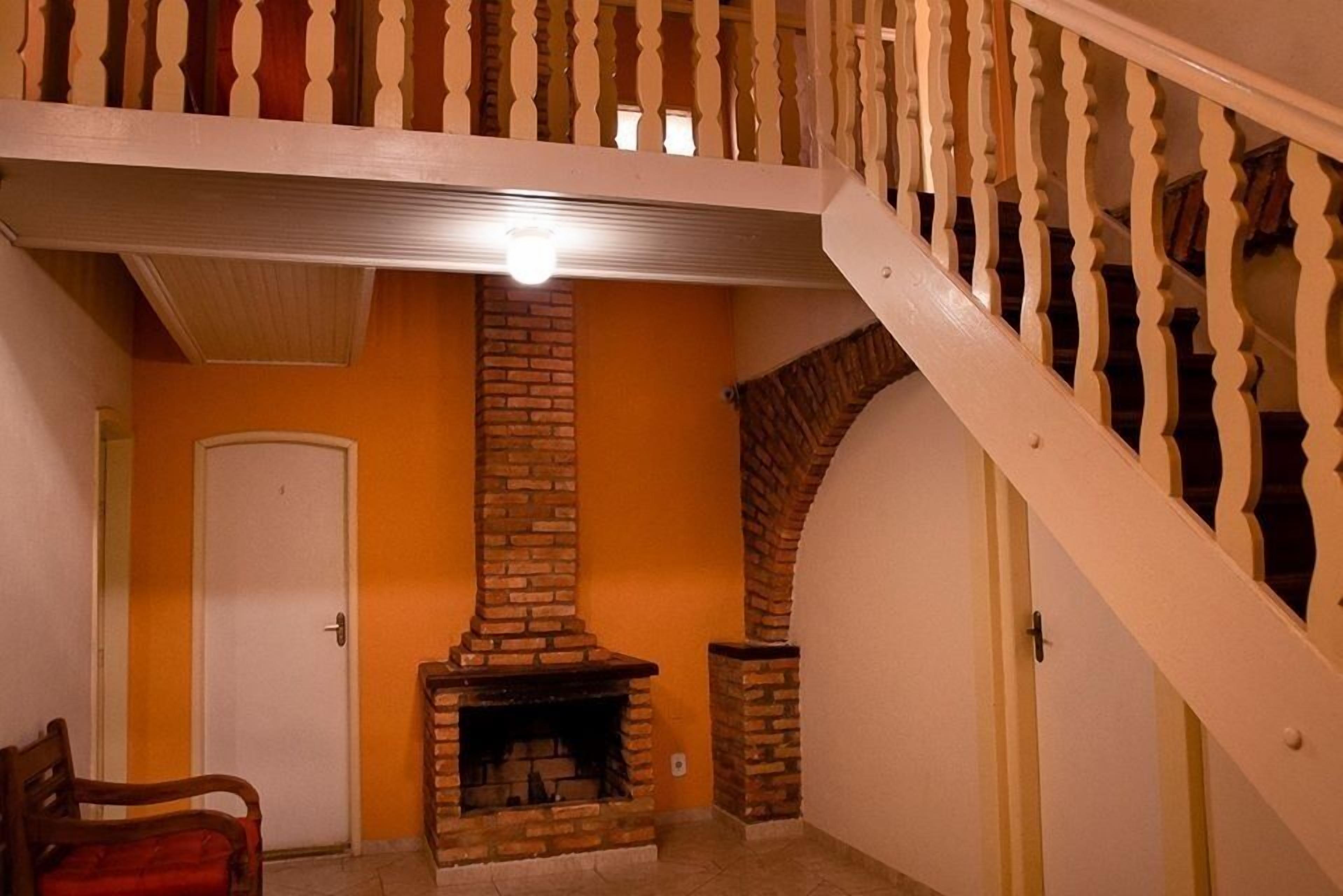 Una habitación con chimenea de ladrillo, una puerta blanca y una escalera de madera.