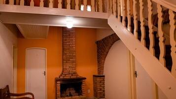 Una habitación con chimenea de ladrillo, una puerta blanca y una escalera de madera.