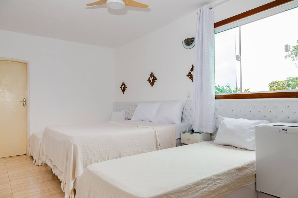 Une chambre avec deux lits, un ventilateur de plafond, une fenêtre avec des rideaux et une table de chevet avec une lampe.