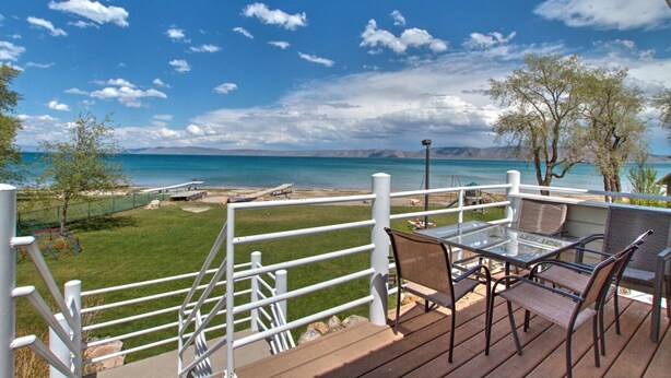A deck with a glass table and chairs overlooking a beach with a clear sky. - Spinnaker Point #1 - Why rent near the beach in Bear Lake when you can rent ON the beach!? (Garden City)