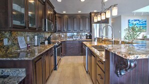 A kitchen with dark wood cabinets, granite countertops, stainless steel appliances, and a modern chandelier. - Spinnaker Point #1 - Why rent near the beach in Bear Lake when you can rent ON the beach!? (Garden City)