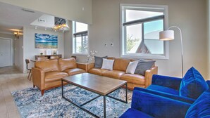 A spacious living room with a brown leather sectional sofa, a blue velvet sofa, a wooden coffee table, and a large window providing natural light. - Spinnaker Point #1 - Why rent near the beach in Bear Lake when you can rent ON the beach!? (Garden City)
