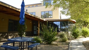 An outdoor patio area with a covered seating area, a building with large windows, and a pathway. - Thunderbird Executive Inn and Conference Center (Glendale)