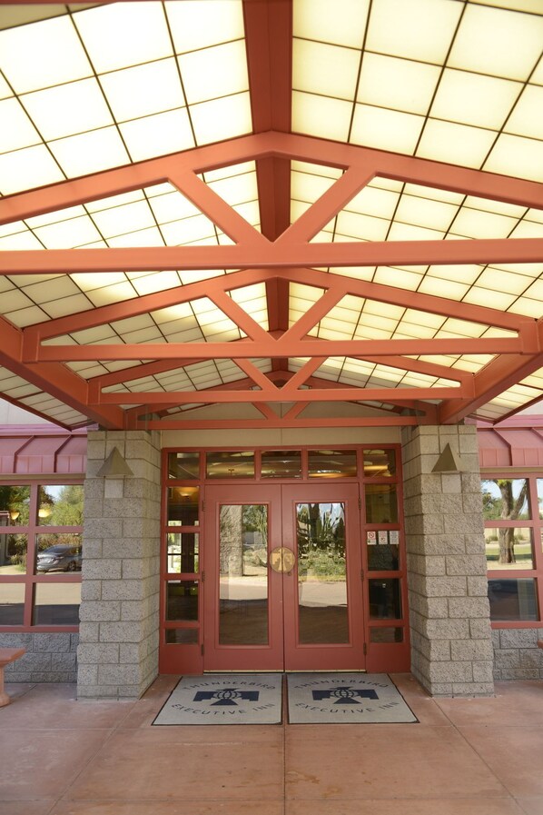 A hotel entrance with a red and beige color scheme, featuring a glass door with a bronze-colored frame, a brick pillar, and a tiled ceiling.