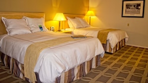 A hotel room with two beds, each with a lamp, a framed picture on the wall, and a patterned carpet. - Thunderbird Executive Inn and Conference Center (Glendale)