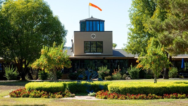 A building with a flag on top, surrounded by well-maintained hedges and flowering plants. - Thunderbird Executive Inn and Conference Center (Glendale)