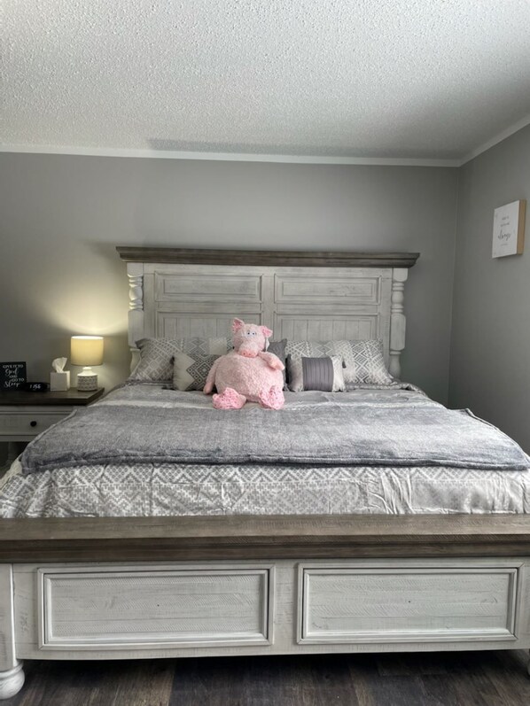 Une chambre à coucher avec un lit, des oreillers, une table de chevet, une lampe et un jouet en peluche.
