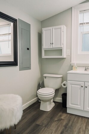 Un baño con inodoro, tocador con armarios, espejo y ventana.