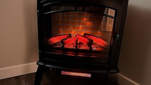 Lareira a lenha num canto de um quarto com soalho de madeira.