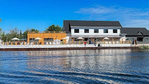 En fastighet vid vattnet med en stor byggnad, en träterrass och en brygga som sträcker sig ut i vattnet.