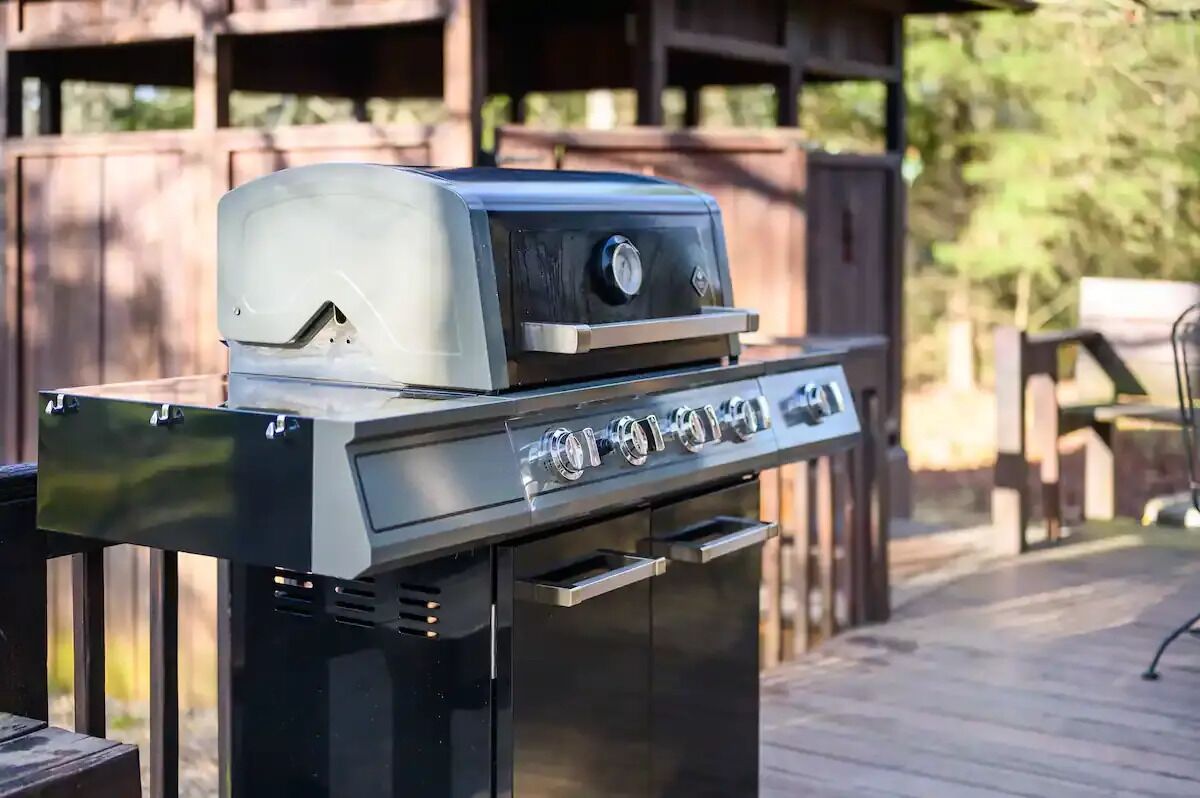 Una parrilla para barbacoa con pantalla digital y perillas de control, ubicada sobre una terraza de madera y con una valla de madera al fondo.
