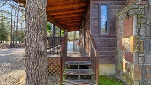 Un rustico chalet con un portico in legno, pareti in pietra e vista sulla foresta circostante.
