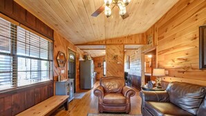 Interno di una baita in legno con una panca di legno, una poltrona in pelle e un divano, una ventola a soffitto e un tappeto.